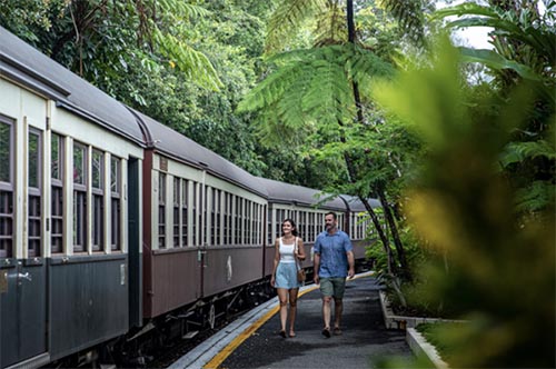Couple walking besides Kuranda train in rainforest 