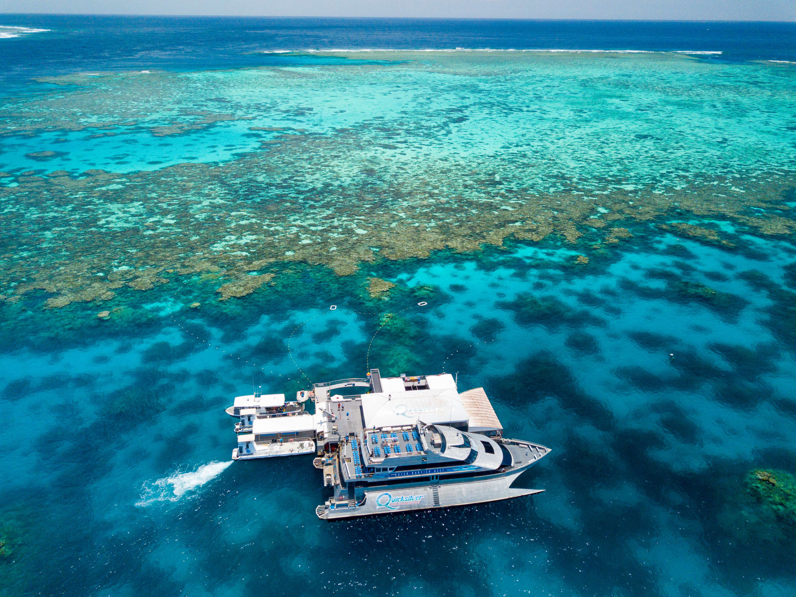 Aerial view of Great Barrier Reef with tour boat and coral formations in clear water