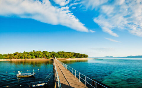 Long pier leading to Green Island with clear blue water and small boats nearby