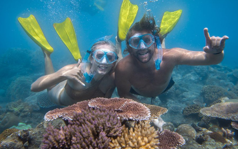 Two snorkelers smiling and swimming above colorful coral with fins and masks