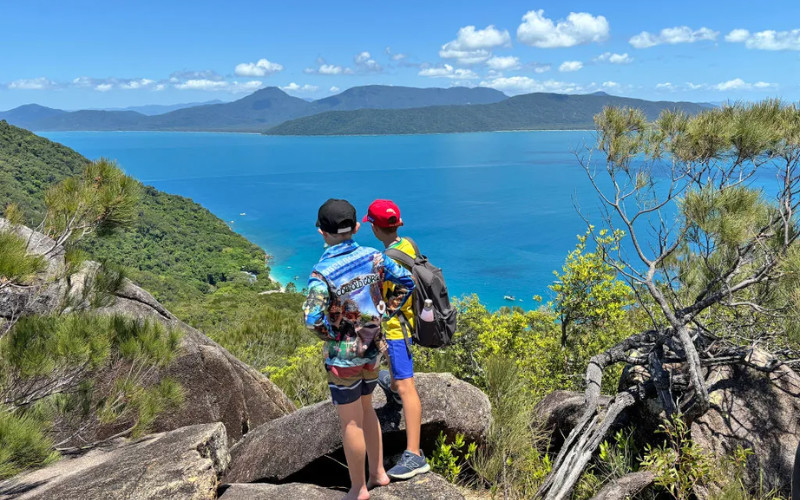 Two kids standing on rocky lookout overlooking blue ocean and tropical coastline