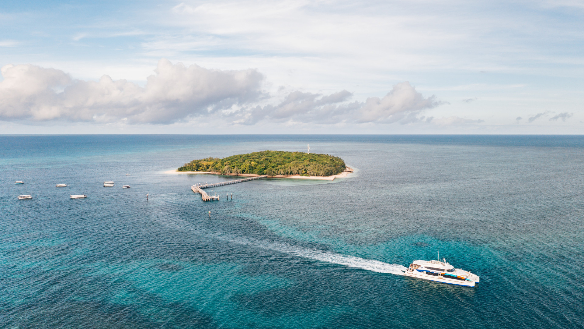 Boat travelling across turquoise ocean toward Green Island with small island and pier visible