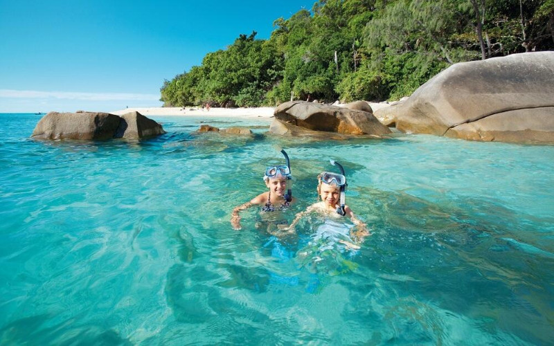 Snorkelers floating in turquoise water near rocky shoreline and tropical beach