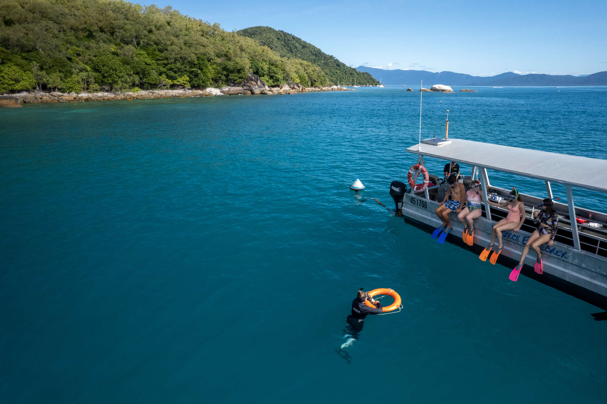 Families snorkelling from a boat in the sheltered waters of Fitzroy Island with rainforest coastline in the background