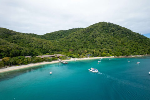 Aerial view of Fitzroy Island's Welcome Bay with the ferry arriving at the jetty and lush rainforest hills