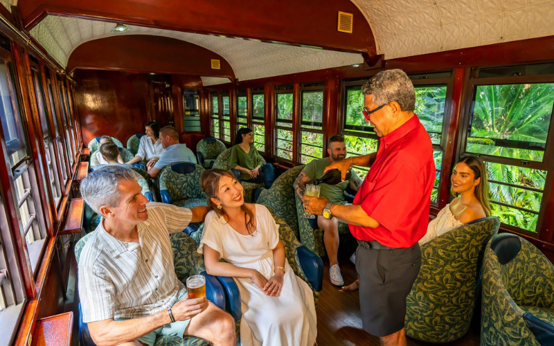 `Kuranda Scenic Railway Gold Class carriage interior with attendant serving passengers drinks and refreshments`