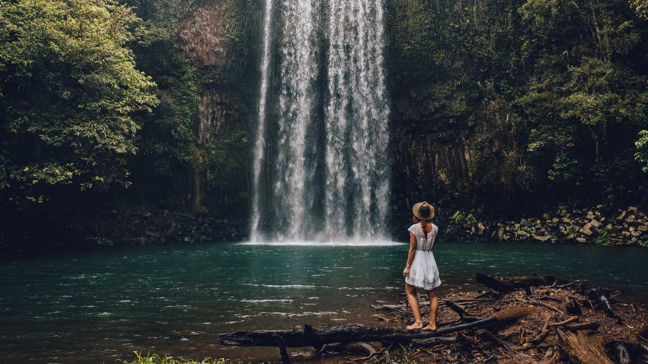 Woman standing beside Millaa Millaa Falls rainforest pool Atherton Tablelands Queensland Australia