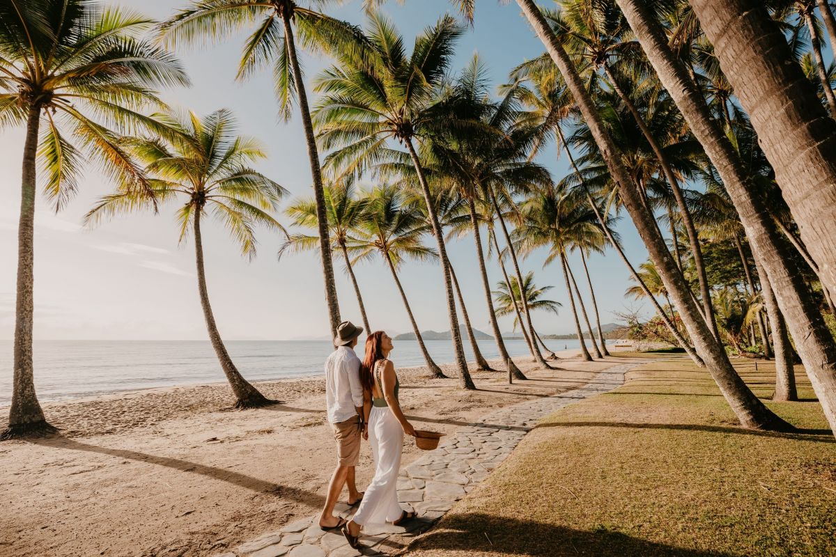 Couple walking along palm-lined esplanade at Palm Cove beach north of Cairns Queensland Australia