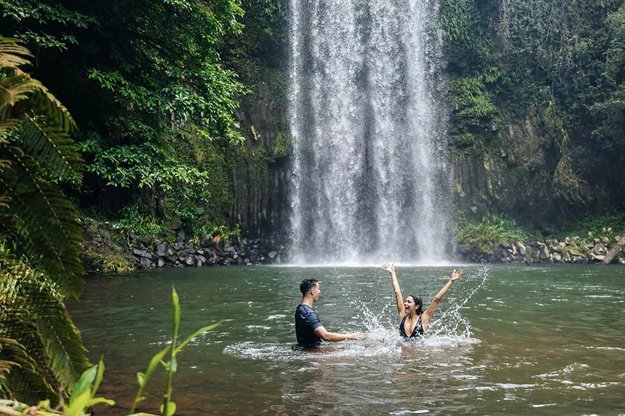 Couple swimming in the natural freshwater pool at the base of Millaa Millaa Falls Atherton Tablelands Queensland