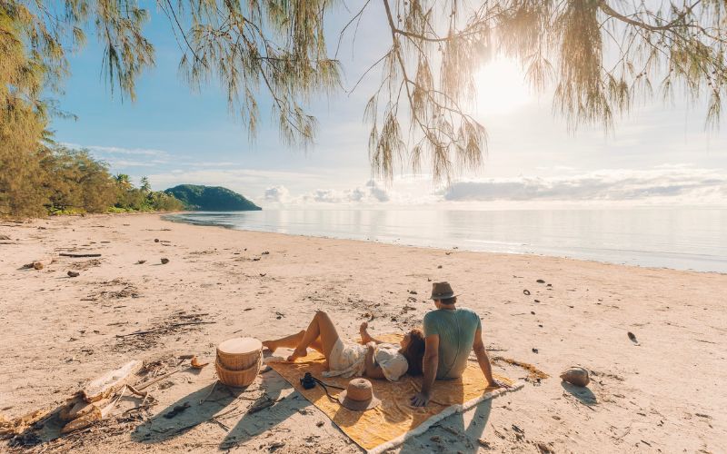 Couple relaxing on Cape Tribulation Beach with rainforest and Coral Sea backdrop Queensland Australia