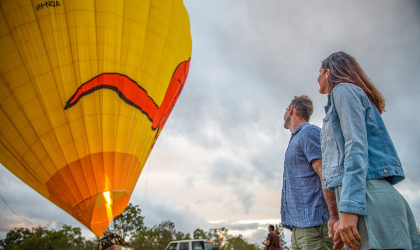 Couple watching a large hot air balloon inflate at dawn before takeoff.