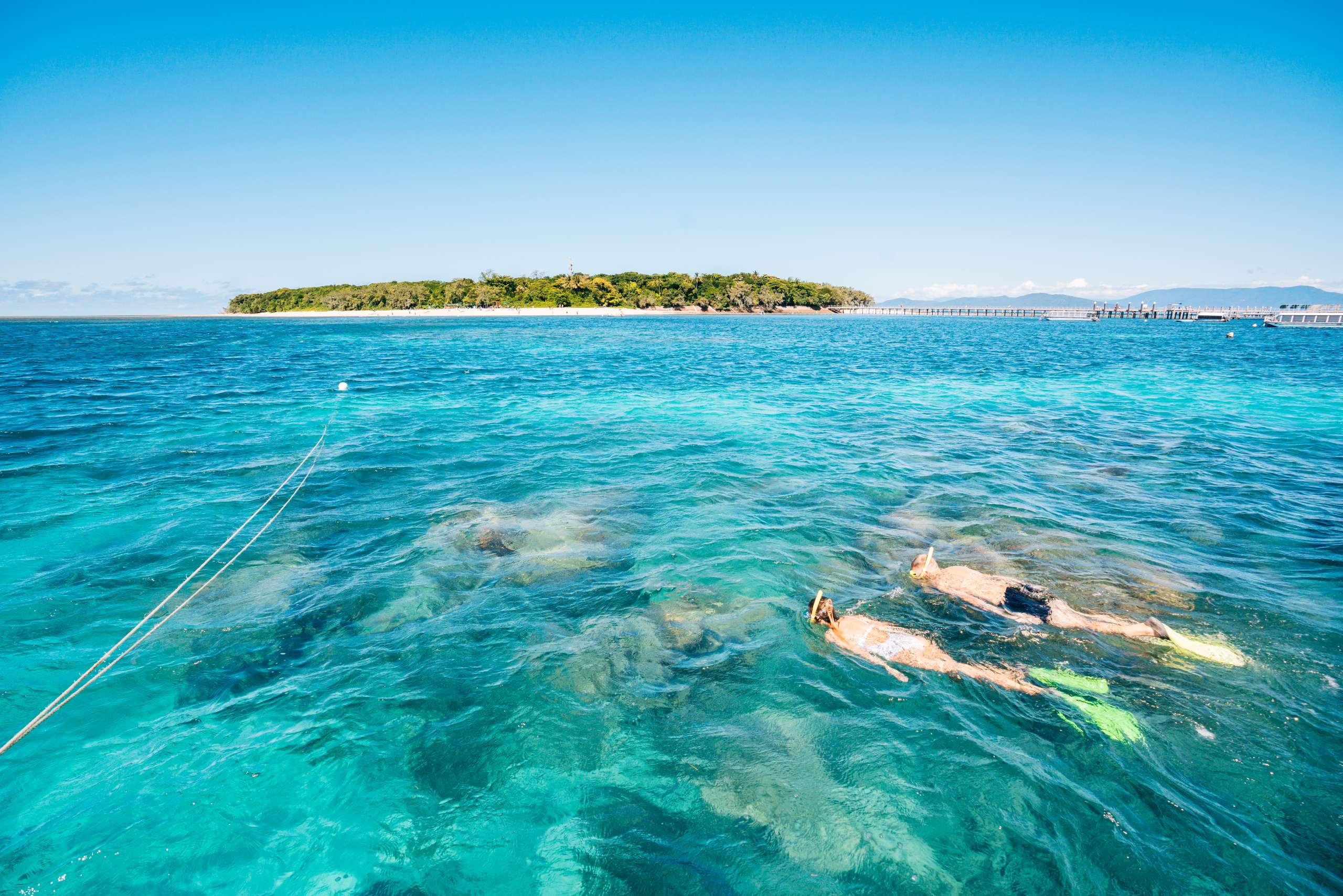 Snorkeler swimming in clear turquoise water near a green, forested island in the distance