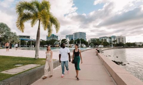 Friends walking along the Cairns Esplanade boardwalk beside the lagoon, with the city skyline in the background.