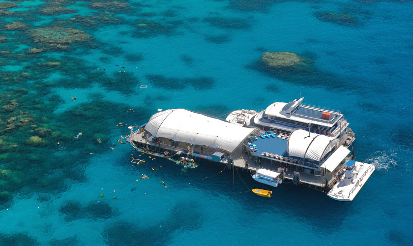 Aerial view of a large reef pontoon with snorkelers in the water, surrounded by turquoise coral reef.