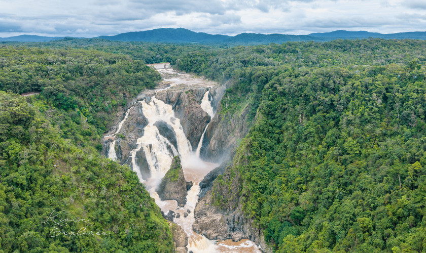 Aerial view of a powerful multi-tiered waterfall cascading through a rainforest gorge surrounded by mountains.