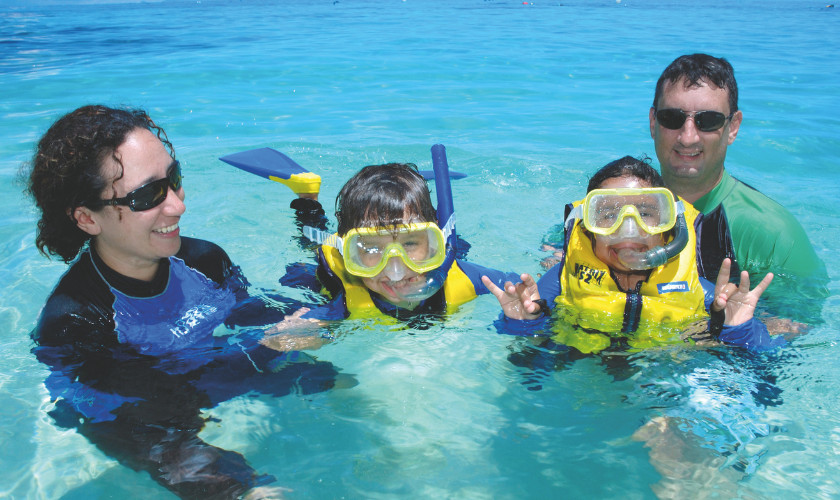 Family of four in stinger suits and life jackets floating together in clear turquoise water.