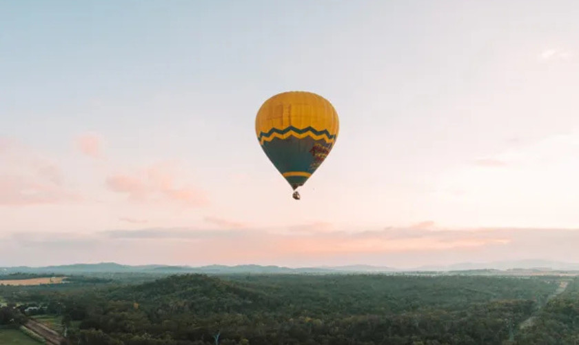 Single hot air balloon drifting over rolling green hills at sunrise.