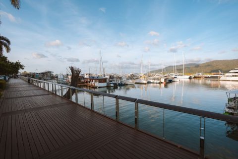 Wooden boardwalk along Cairns marina at dusk with sailboats and tour vessels moored in the harbour