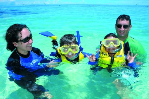 Family with two kids snorkelling in clear turquoise water on a family-friendly reef tour from Cairns