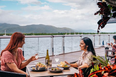 Two women dining at a waterfront restaurant in Cairns with views of Trinity Inlet and the mountains